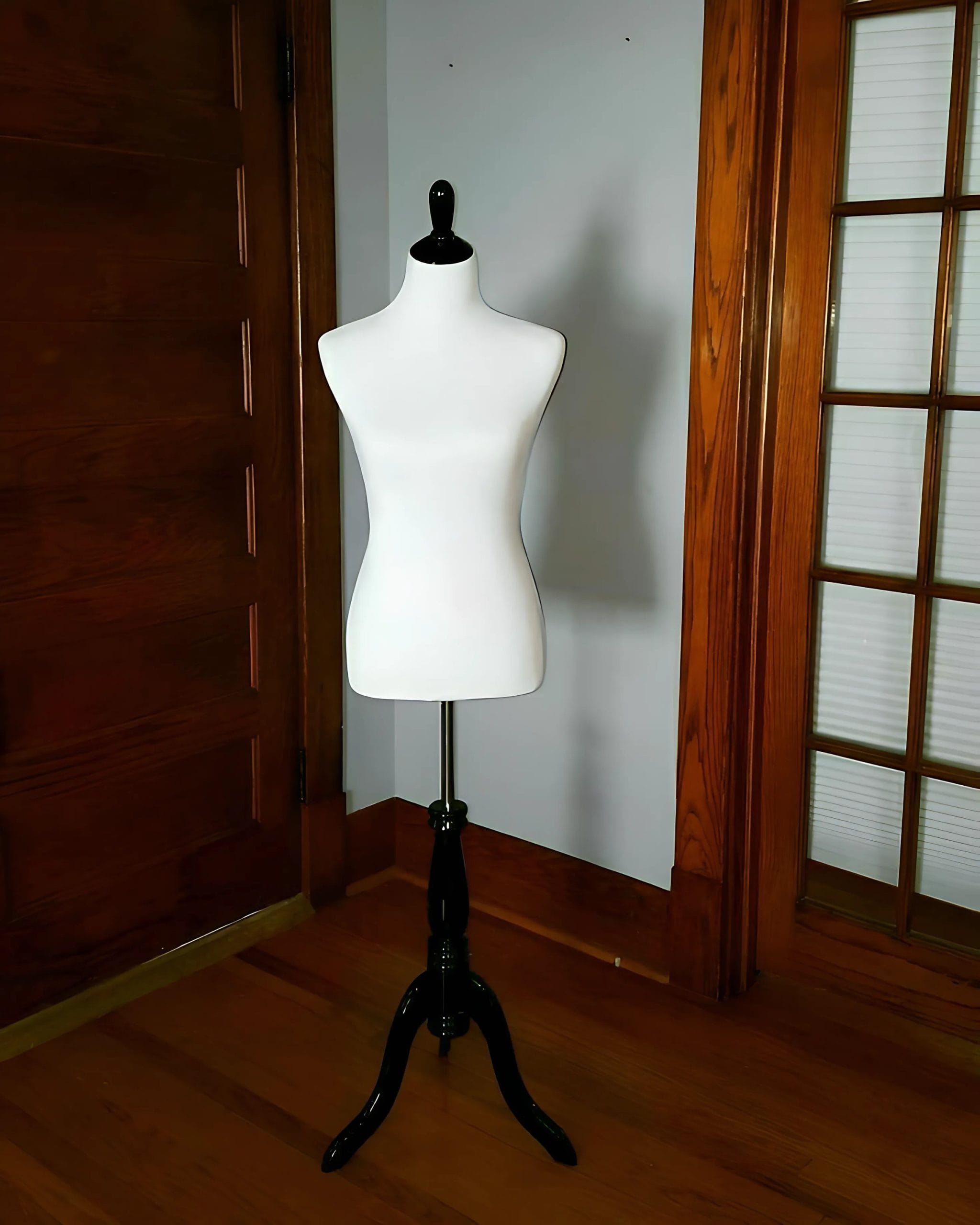 A white dress form on a black stand positioned in a room with wooden features.